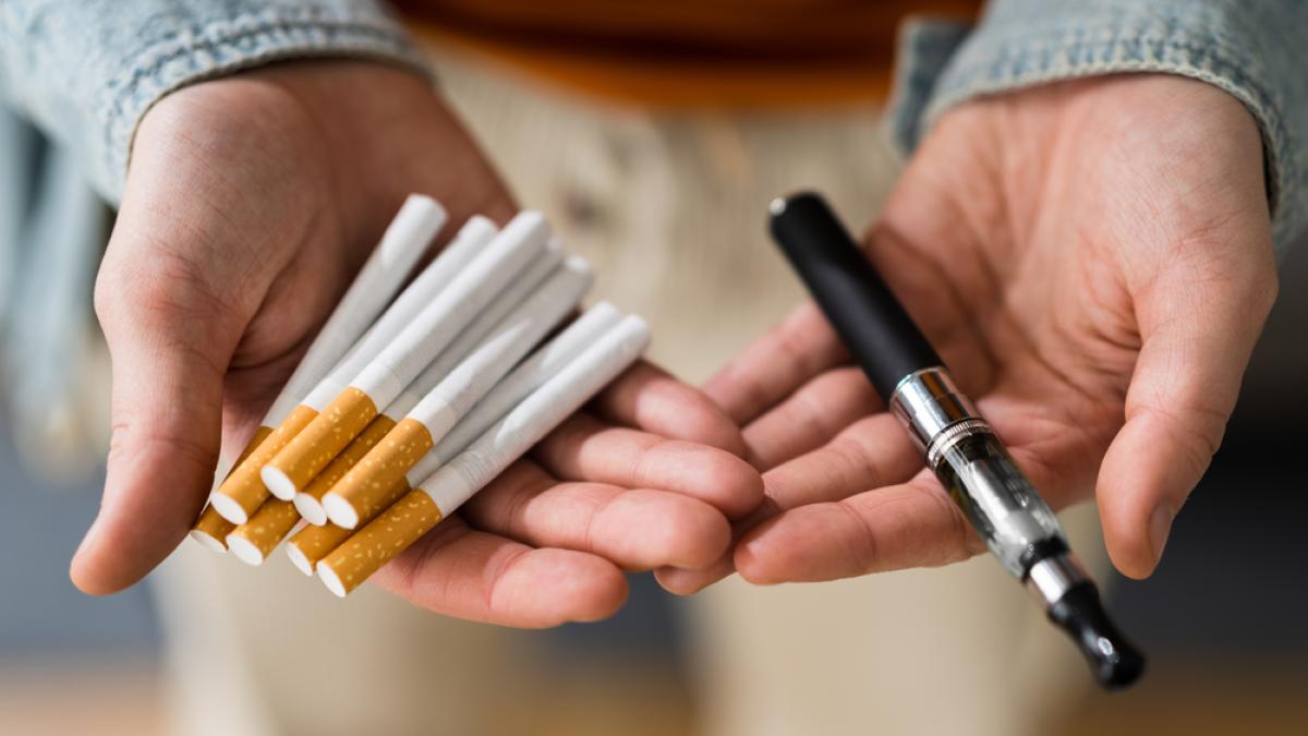 a man holding cigarettes in one hand and a vape in the other