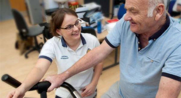 A physio working with a patient on a stationary bike