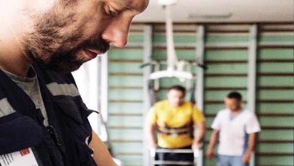 Photo of Physio Pete Skelton with patients in the background gym setting in a hospital in Zaporizhia, Ukraine.[Photo: World Health Organization/Anne Pellichero]